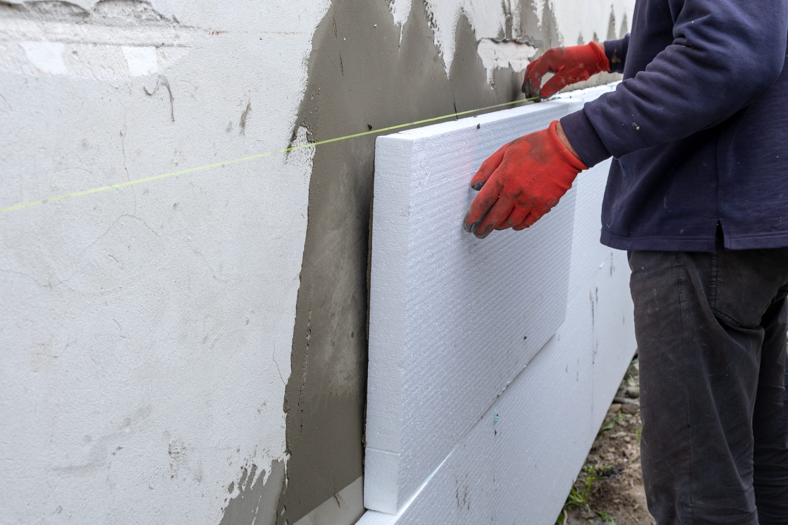 Stavebný špecialista prikladajúci polystyrénovú izoláciu na stenu montovaného drevodomu